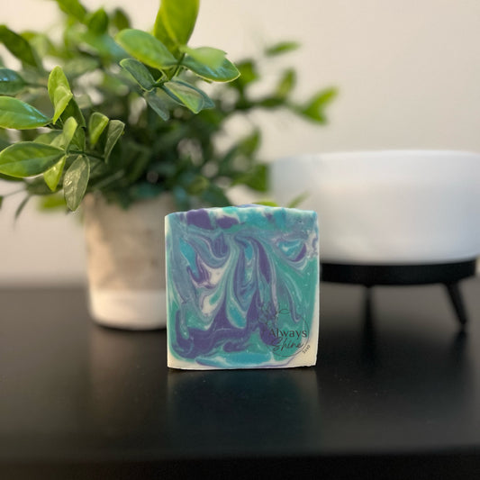 Picture displays a single bar of soap that has swirls of green, teal, navy and white